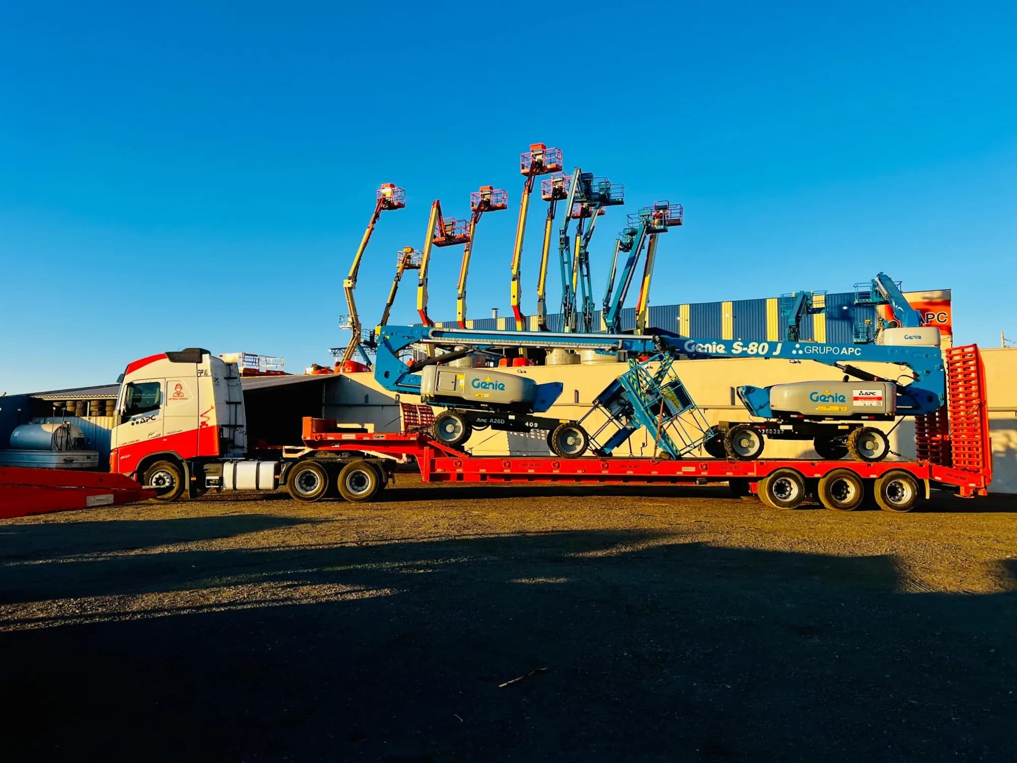 Carreta do Grupo APC carregada com plataformas Genie no pátio da empresa, no fim da tarde