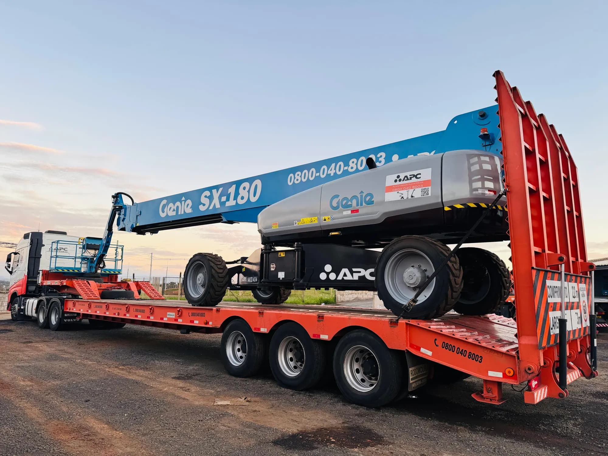 Carreta do Grupo APC com uma plataforma telescópica Genie SX-180 carregada, no fim da tarde
